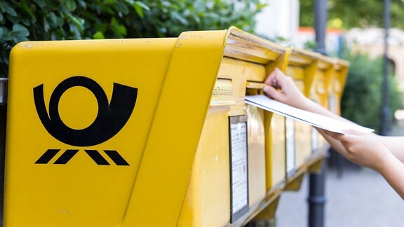 Frau steckt mehrere Brief in einen Briefkasten der Deutschen Post AG