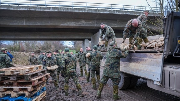 Soldaten der Bundeswehr laden Sandsäcke von einem Lkw, um einen Deich an der Helme zu sichern. 