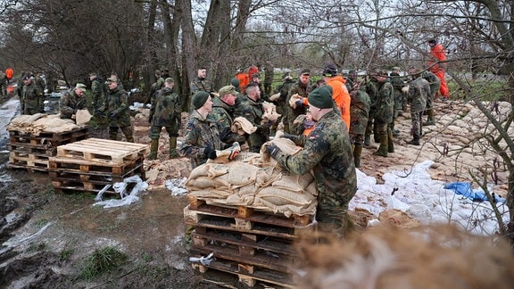 Soldatinnen und Soldaten der Bundeswehr sichern einen Deich an der Helme mit Sandsäcken. 