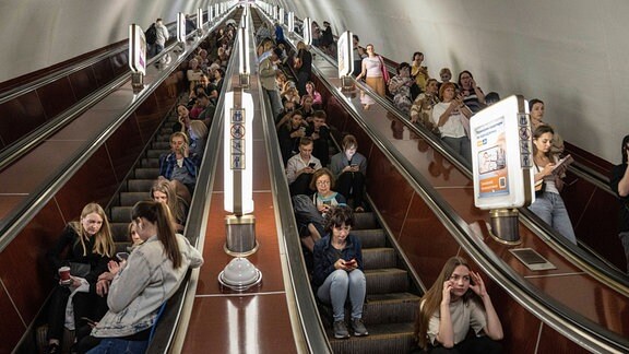 Menschen sitzen auf einer Rolltreppe, während sie in einer Metrostation Schutz suchen.