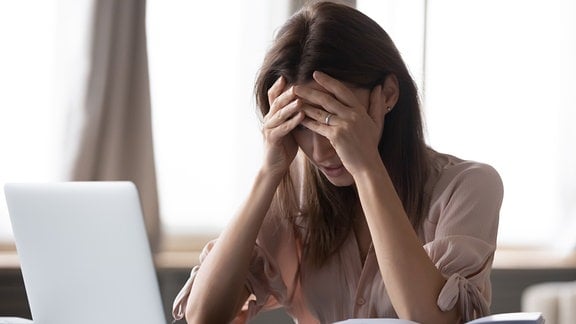 Frustrierte, gestresste Frau am Laptop hält Kopf in die Hände gestützt.
