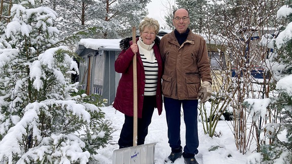 Das Ehepaar Just steht mit einem Schneeschieber auf einem Campingplatz.