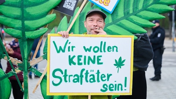 "Wir wollen keine Straftäter sein!" steht auf dem Plakat eines Joint rauchenden Demonstranten für die Entkriminalisierung von Cannabis am Brandenburger Tor in Berlin, am 20. April 2023
