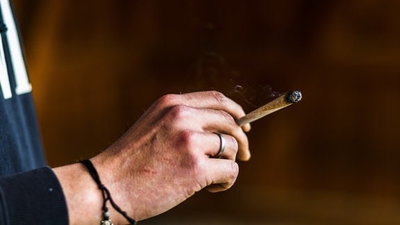 Ein Cannabis-Patient hält einen brennenden Joint in der Hand.