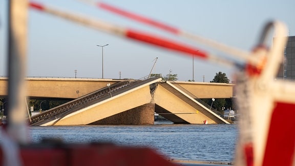 Ein Absperrband rahmt die teileingestürzte Carolabrücke am Ufer der Elbe.