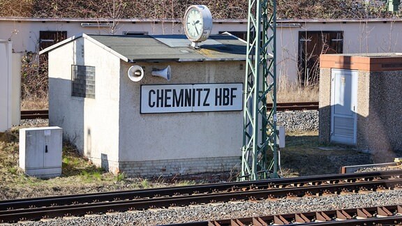 Ein Schild "Chemnitz HBF" hängt an einem kleinen Häuschen neben den Gleisen. 