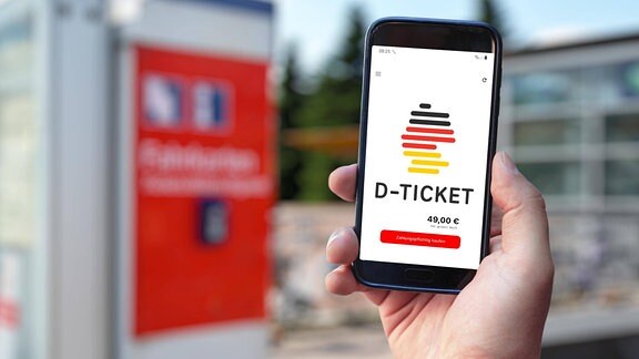 Symbolbild: Im Hintergrund ein roter Fahrkartenautomat der Bahn. Im Vordergrund ein Smartphone, auf dem Bildschirm: "D-Ticket"
