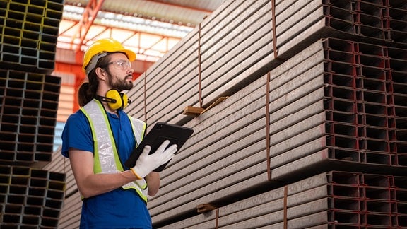 Lagerarbeiter mit Helm und Tablet in einem Industrielager.