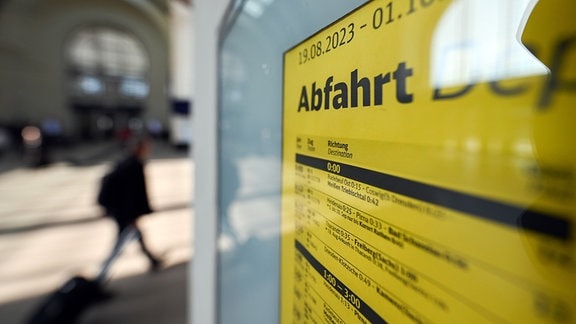 „Abfahrt“ ist auf einem Fahrplan auf dem Hauptbahnhof zu lesen. Im Hintergrund läuft ein Mann vorbei.