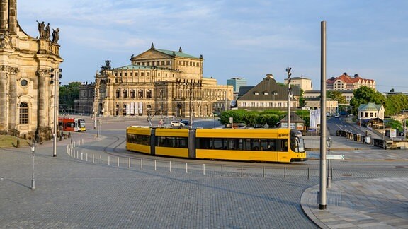 Eine Straßenbahn der Dresdner Verkehrsbetriebe (DVB) fährt am Morgen in der Altstadt über den Theaterplatz an der Hofkirche (l) und der Semperoper entlang.