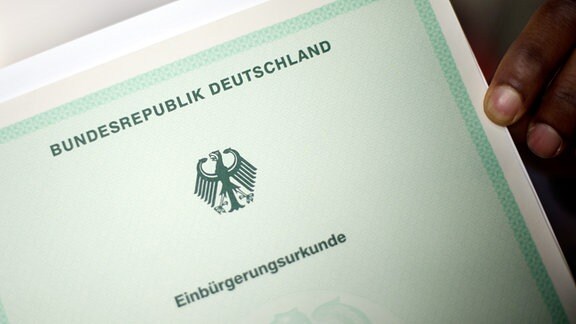 Ein Mann hält bei einer Einbürgerungszeremonie eine Einbürgerungsurkunde der Bundesrepublik Deutschland in der Hand. 
