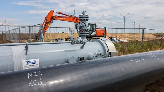 Die Rohre einer künftigen Wasserstoffleitung liegen vor der Kulisse eines Windparks. Am selben Tag (21. Juni) erfolgte hier der Spatenstich für ein Vorzeigeprojekt der Energiewende in Deutschland. 