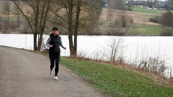 Eine Frau joggt an einem Seeufer entlang