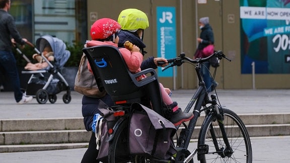 Eine Frau schiebt ihr Fahrrad mit ihrem Kind drauf.