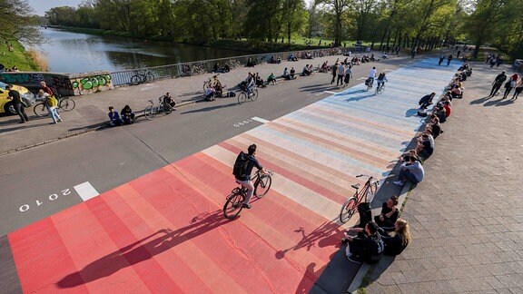 Menschen sitzen neben so genannten "Warming Stripes" auf der Sachsenbrücke. 