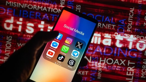 Illustration - Social-Media-Symbole auf einem Smartphone mit Desinformation auf dem Bildschirm im Hintergrund