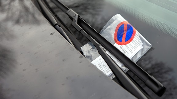 Ein Knöllchen ist an einem Fahrzeug auf einem Parkplatz an dem Scheibenwischer angebracht. 
