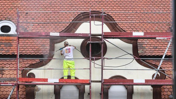 Ein Maler reinigt die eingeruestete Fassade eines Altbaus aus der Gruenderzeit mit einem Hochdruckreiniger