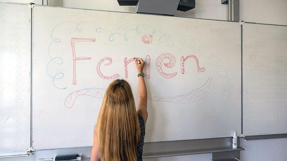 Eine Lehrerin des Wilhelm-Hausenstein-Gymnasium schreibt das Wort «Ferien» an die Klassentafel. 