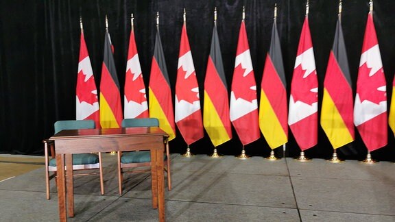 Die Flaggen von Kanada und Deutschland hinter einem Tisch mit Stühlen.