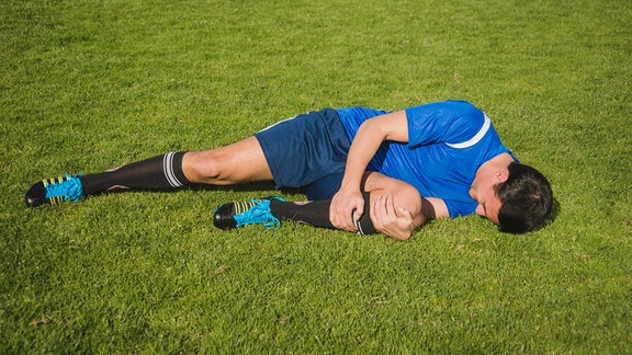 Gestelltes Foto eines verletzten Fußballspielers am Boden.