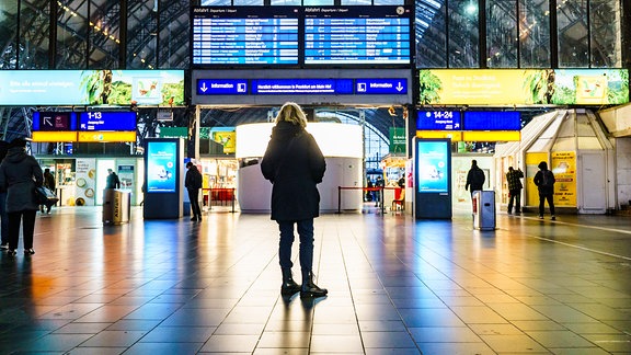 Eine Frau informiert sich an einer großen Anzeigetafel im Hauptbahnhof.