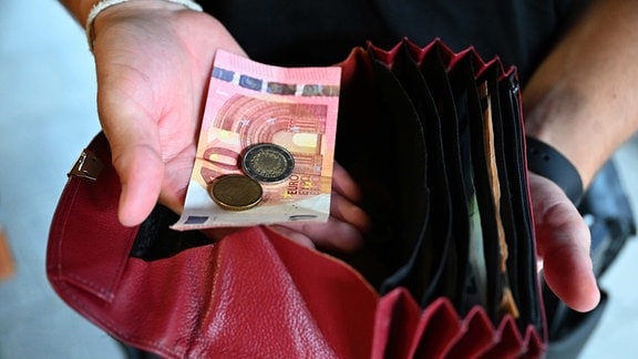 Ein Kellner eines Restaurants hält einen Geldbeutel in der Hand, während er in der anderen Hand Bargeld hält.