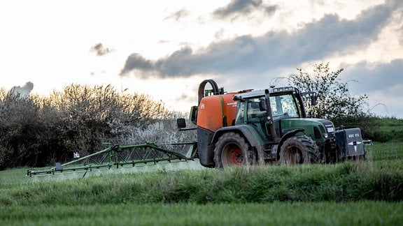 Ein Landwirt bringt mit seinem Traktor und einer großen Pflanzenschutzspritze ein hochwirksames Pflanzenschutzmittel auf das Feld aus.