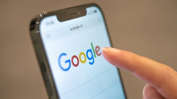 Eine Frau hält ihr Handy in der Hand, auf dem die Google-Seite im Browser zu sehen ist. 