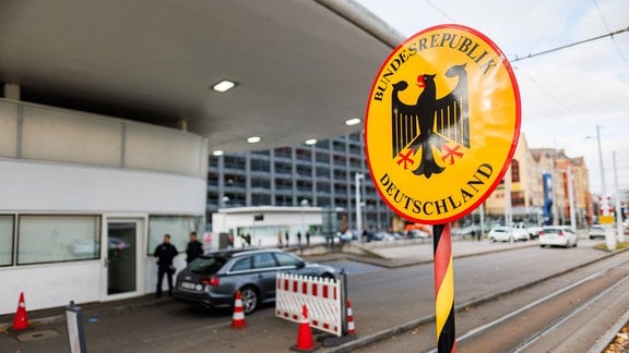 Ein Grenzschild steht am Grenzübergang in Weil am Rhein-Friedlingen während im Hintergrund zwei Beamte der Bundespolizei zu sehen sind. Die Bundespolizei kontrolliert derzeit verstärkt Reisende, so auch an der Grenze zur Schweiz. Bundesinnenministerin Faeser (SPD) hatte stationäre Grenzkontrollen an den Grenzen zu Polen, Tschechien und der Schweiz am 16. Oktober zunächst für zehn Tage angemeldet und dann mehrfach verlängert. Sie begründete diesen Schritt mit dem Bekämpfen von irregulärer Zuwanderung und Schleuserkriminalität.