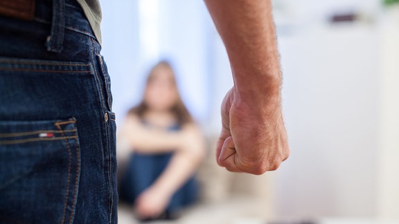 Ein Mann ballt in einem Wohnzimmer in Hamburg seine Hand zur Faust, während eine Frau aengstlich auf der Couch sitzt (gestellte Szene).