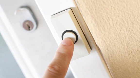 Zeigefinger betätigt eine Klingel neben einer Haustür
