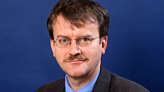 Heiko Kosel, ein Mann mit Anzug, Schnauzbart und Brille.