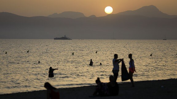 Menschen halten sich während die Sonne untergeht am Strand von Arenal auf.