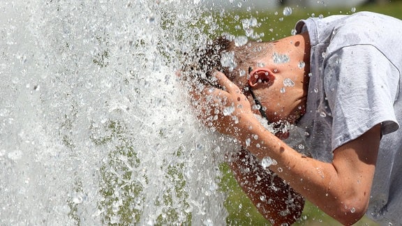 Bei Temperaturen um 29 Grad Celsius erfrischt sich ein junger Mann im Berliner Lustgarten am Wasser eines Brunnens