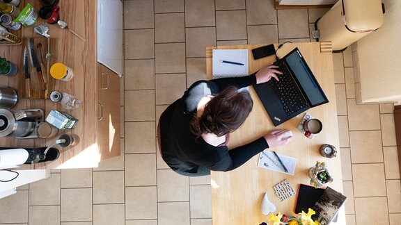 Eine Frau sitzt in einer Küche im Homeoffice am Tisch und arbeitet an einem Laptop (gestellte Szene).