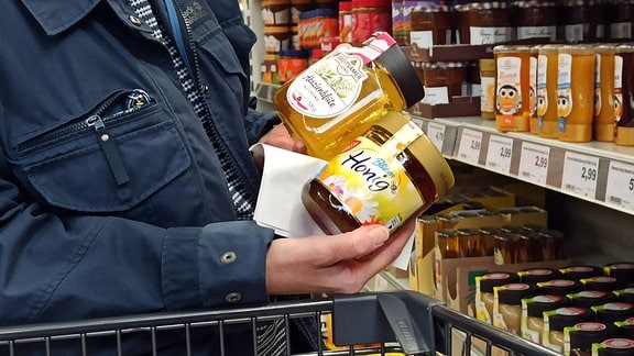 Eine Frau vergleicht im Supermarkt zwei Sorten Honig.