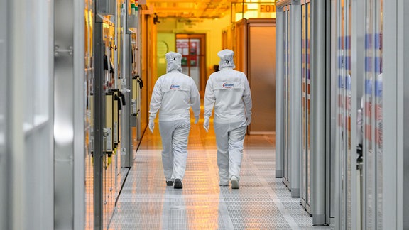 Mitarbeiterinnen des Chipkonzerns Infineon laufen im Reinraum der Chipfabrik entlang.