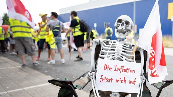 «Die Inflation frisst mich auf» steht während eines Warnstreiks vor dem Ikea-Verwaltungssitz und der Filiale auf einem Skelett.