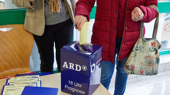 Eine Wählerin (r) steckt einen Fragebogen in eine zusätzliche "Wahlurne" der Infratest dimap für die Wahlprognose der ARD zur Bürgerschaftswahl im Eingangsbereich eines Wahllokals