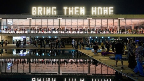 Menschen stehen unter einer Leuchtschrift mit dem Text "Bring Them Home" («Bringt sie nach Hause»), bei einer Demonstration, die die Rückkehr der Geiseln fordert, die bei dem Hamas-Angriff vom 07.10.2023 in Israel entführt wurden.