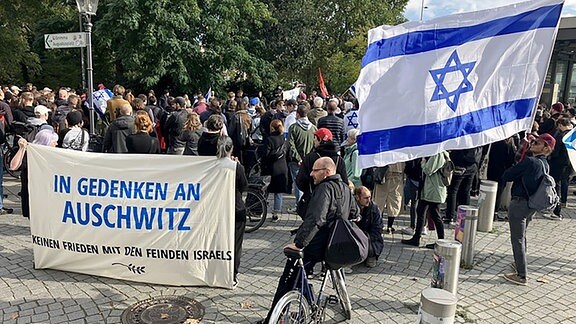 Eine israelische Fahne und ein Transparent mit der Aufschrift "In Gedenken an Auschwitz, kein Frieden mit den Feinden Israels" tragen Teilnehmer einer Kundgebung in Leipzig.