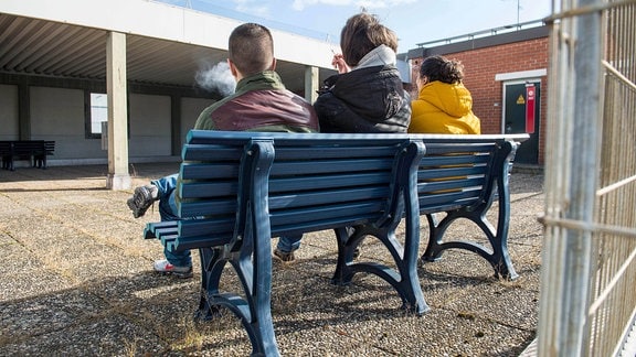 Drei junge Menschen sitzen auf einer Bank.