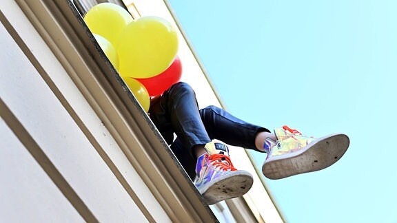 Beine und Luftballons werden aus einem Fenster gehalten.