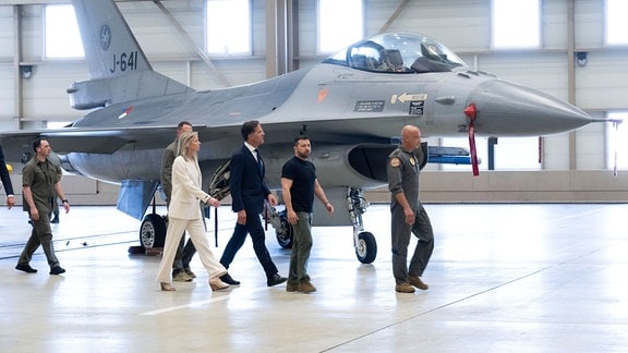 Wolodymyr Selenskyj (2.v.r), Präsident der Ukraine, und Mark Rutte (M), Ministerpräsident der Niederlande, laufen an einem F-16 Kampfjet vorbei.
