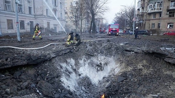 Feuerwehrleute arbeiten in der Nähe eines Kraters nach russischen Angriffen.