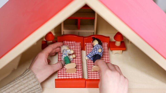 Zwei hände halten zwei Puppen in einem Puppenhaus.