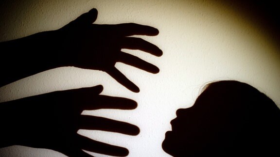 Schatten von Händen einer erwachsenen Person und der Kopf eines Kindes an einer Wand eines Zimmers