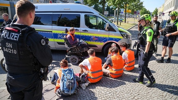 Polizisten stehen um Mitglieder der Protestgruppe Letzte Generation nach einer Sitzblockade auf dem Leipziger Georgiring