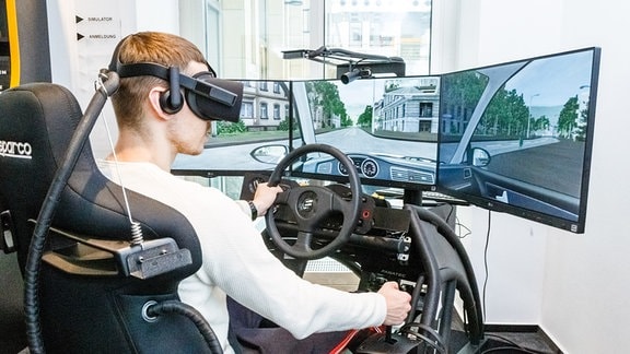 Junger Mann sitzt mit VR-Brille in einem Fahrsimulator und übt Autofahren